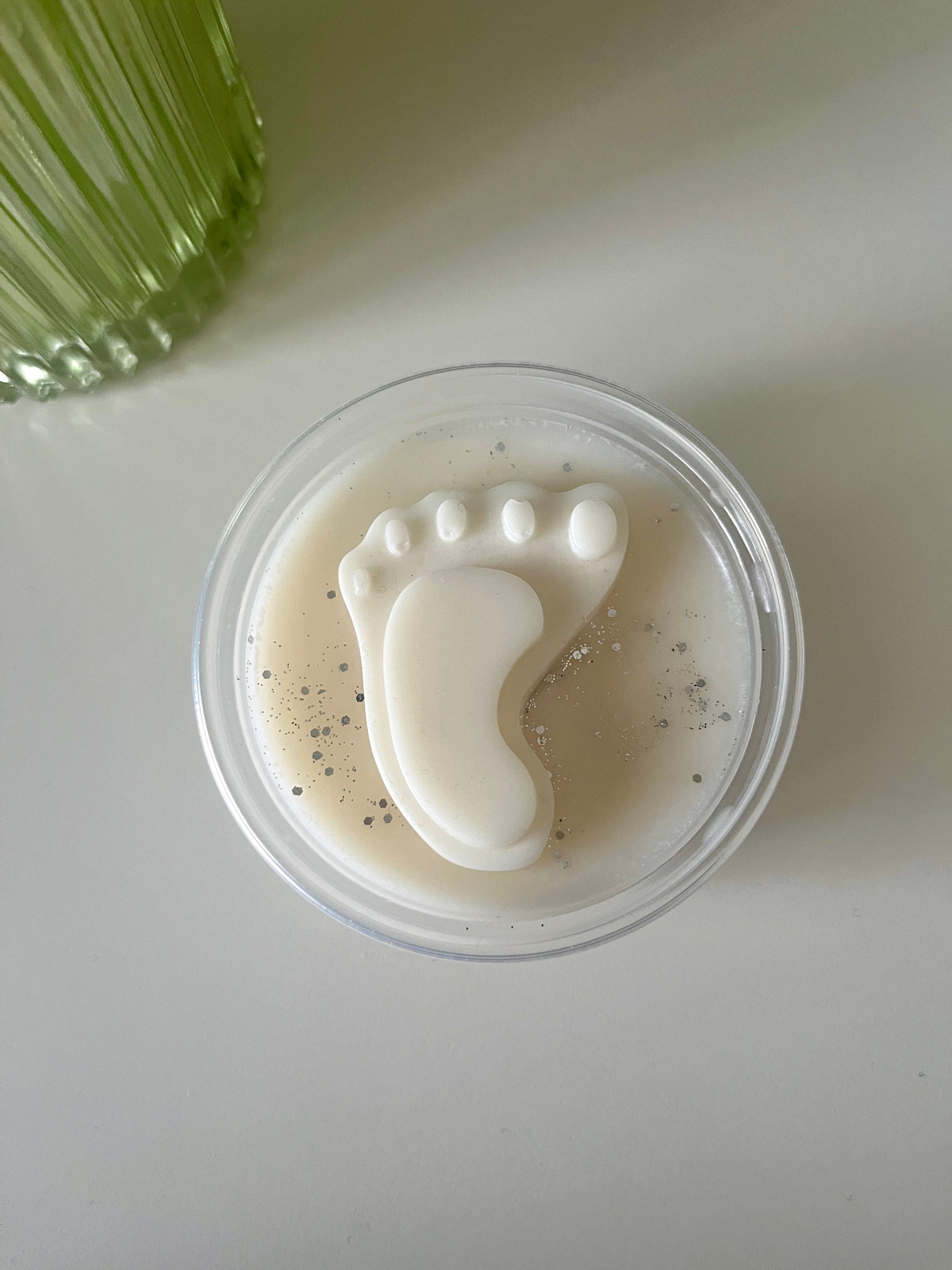 A pot of white wax topped with a white wax baby foot and silver glitter