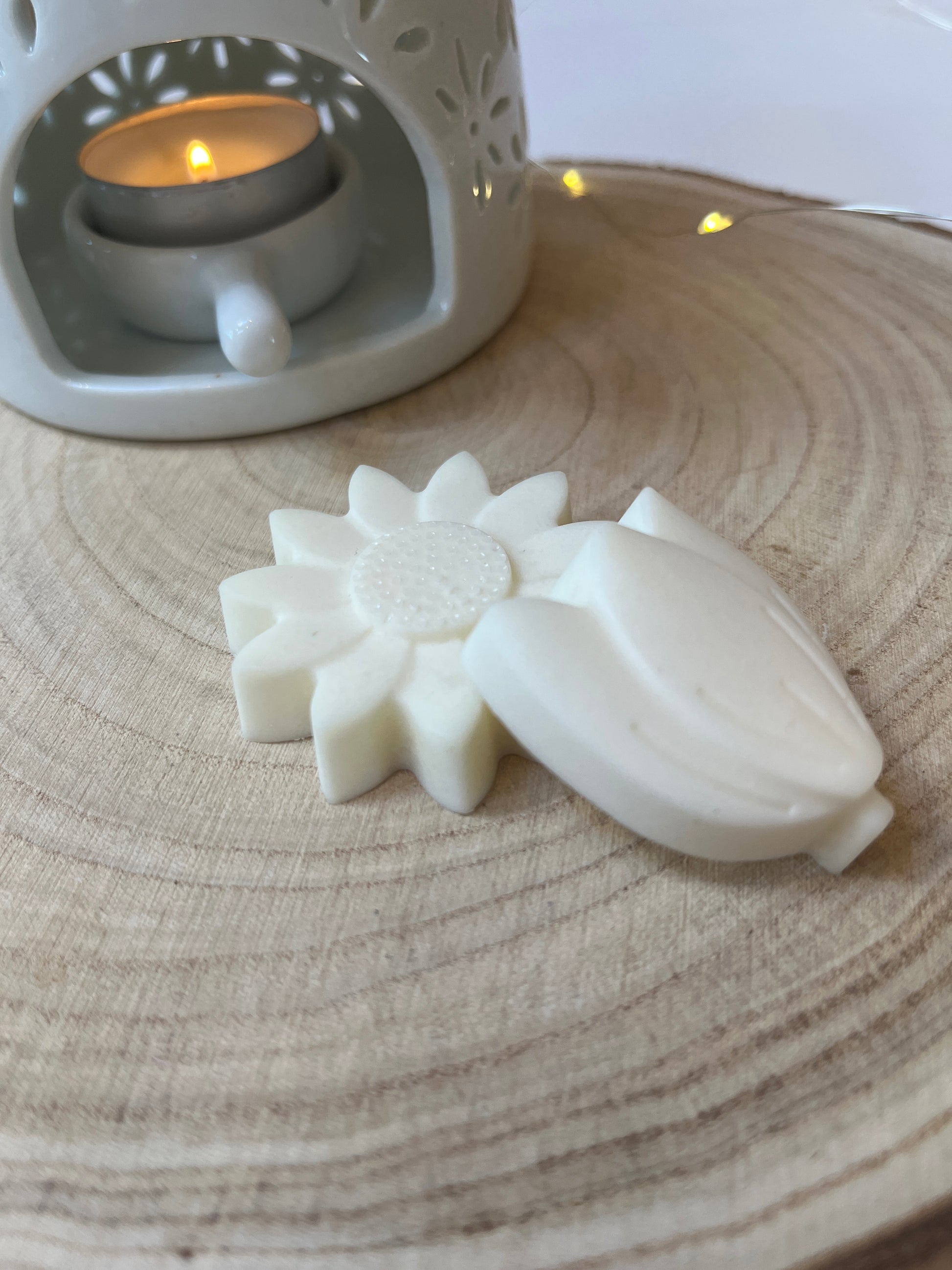 Two white wax flowers on a log disc with a wax melt burner in the background