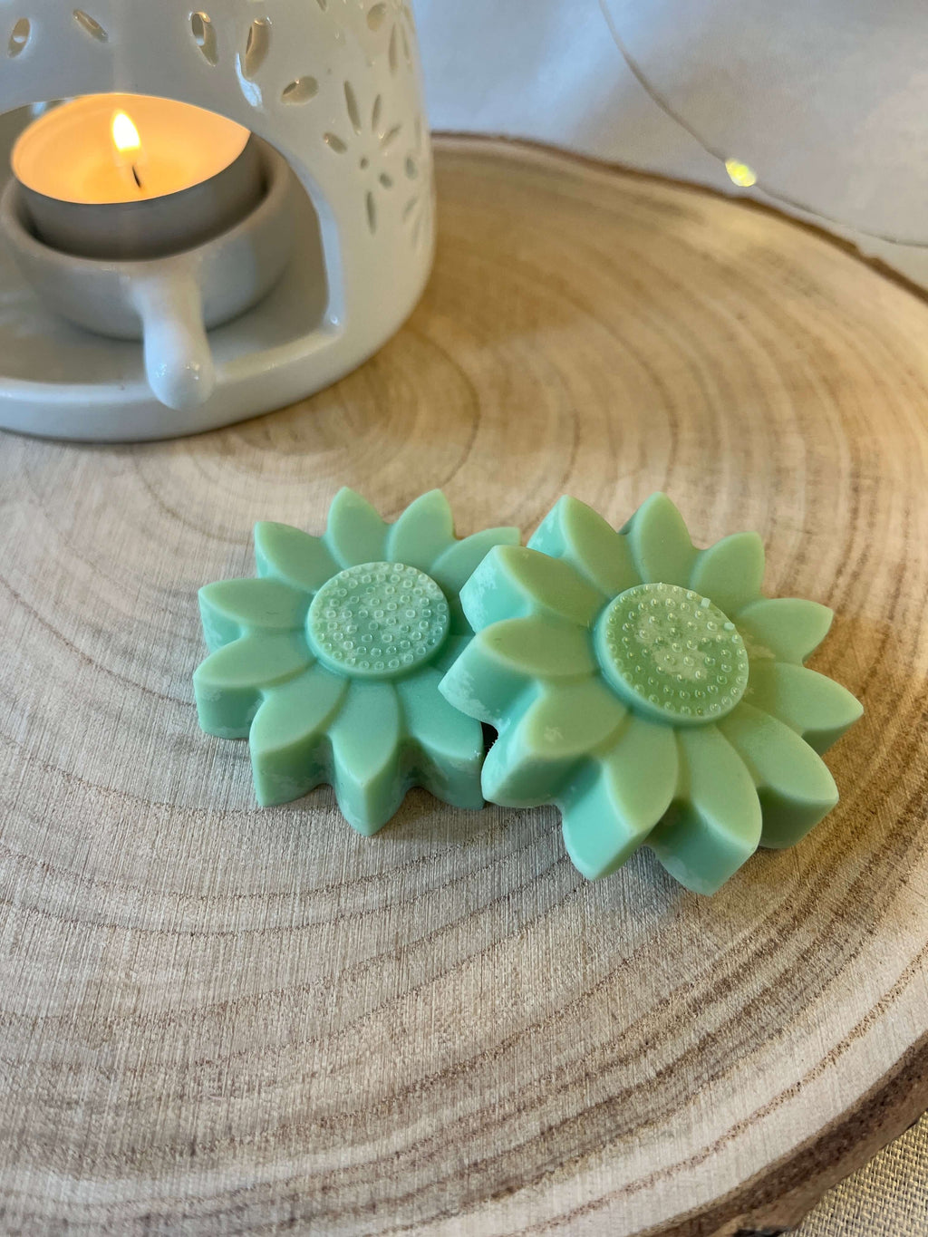 Two green wax flowers on a log disc with a wax melt burner in the background