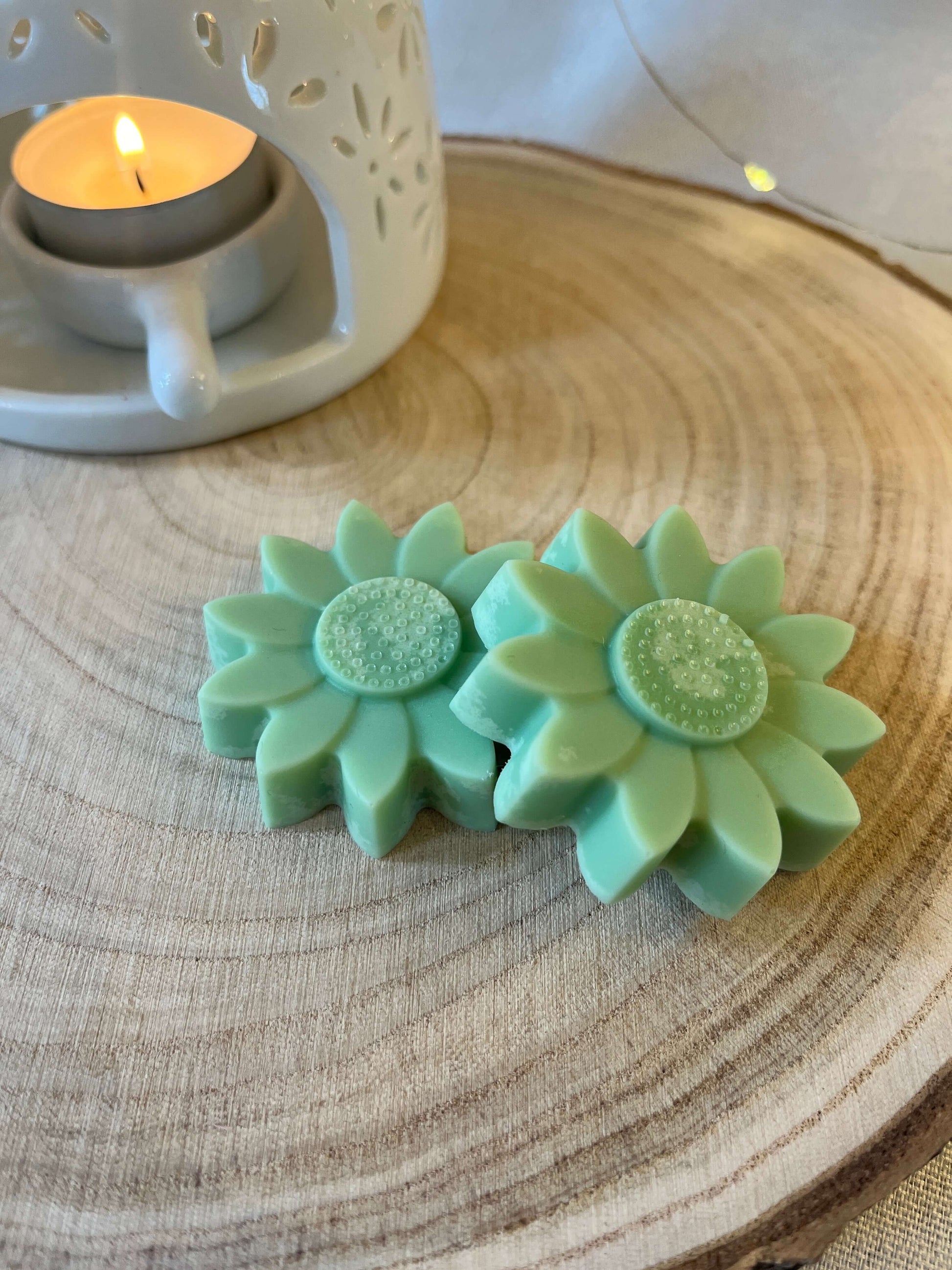 Two green wax flowers on a log disc with a wax melt burner in the background