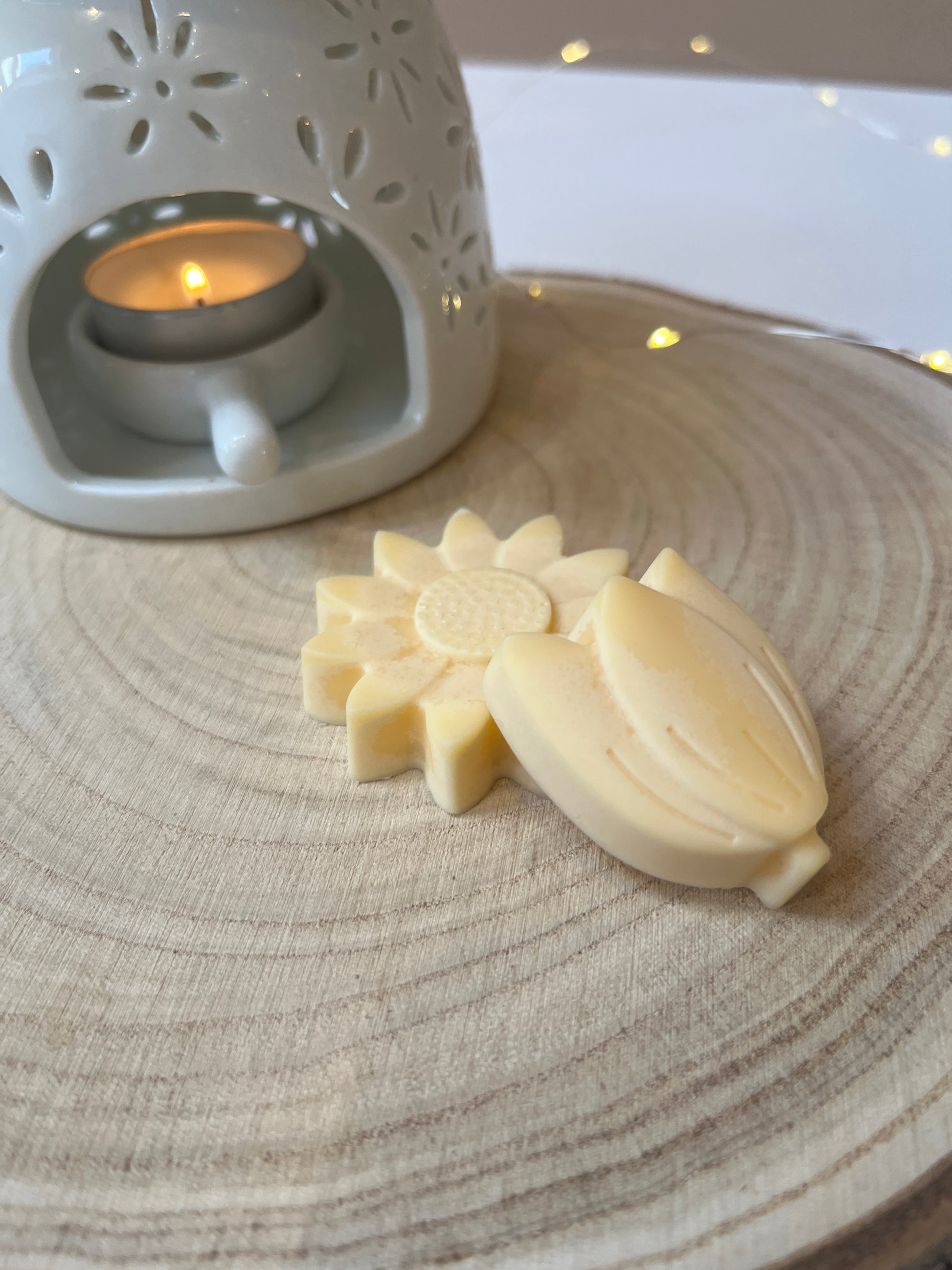 Two yellow wax flowers on a log disc with a wax melt burner in the background